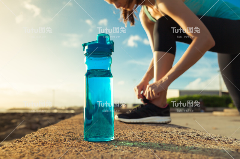 女跑步者系着她的鞋子旁边的一瓶水