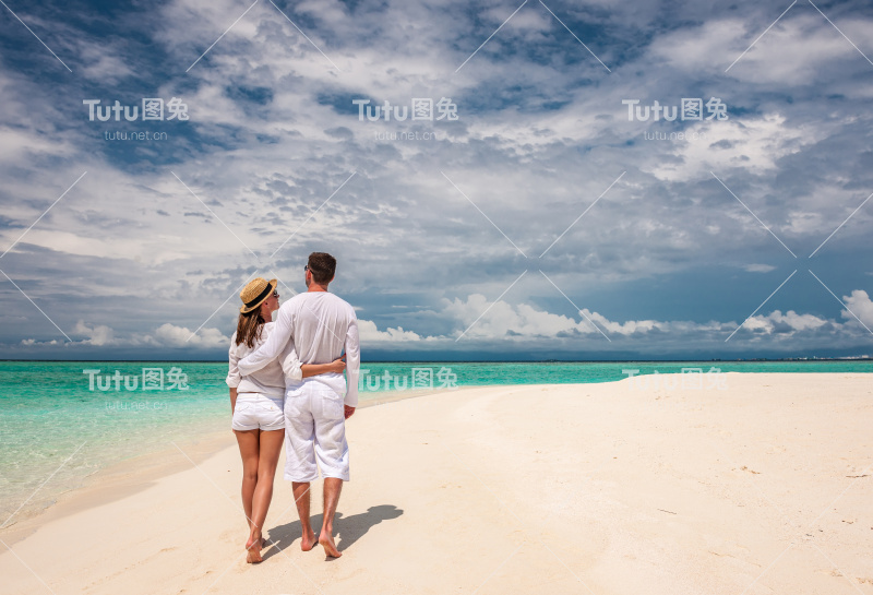 一对穿着白色衣服的夫妇在马尔代夫的海滩上散步