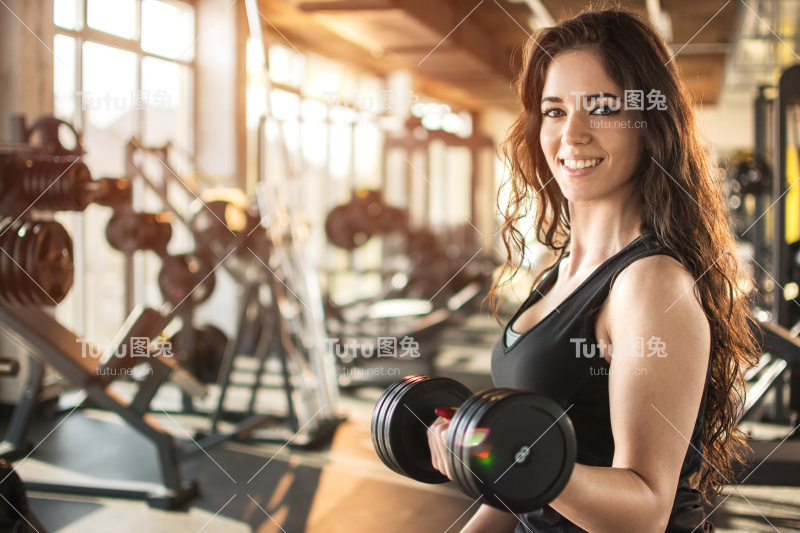 年轻微笑的女人在健身房举重的肖像。