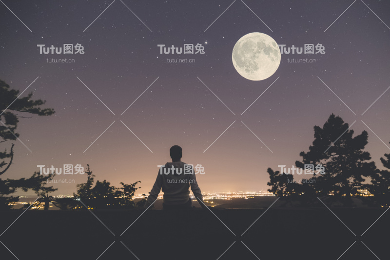 从山上俯瞰城市的景色。天上有满月和星星。