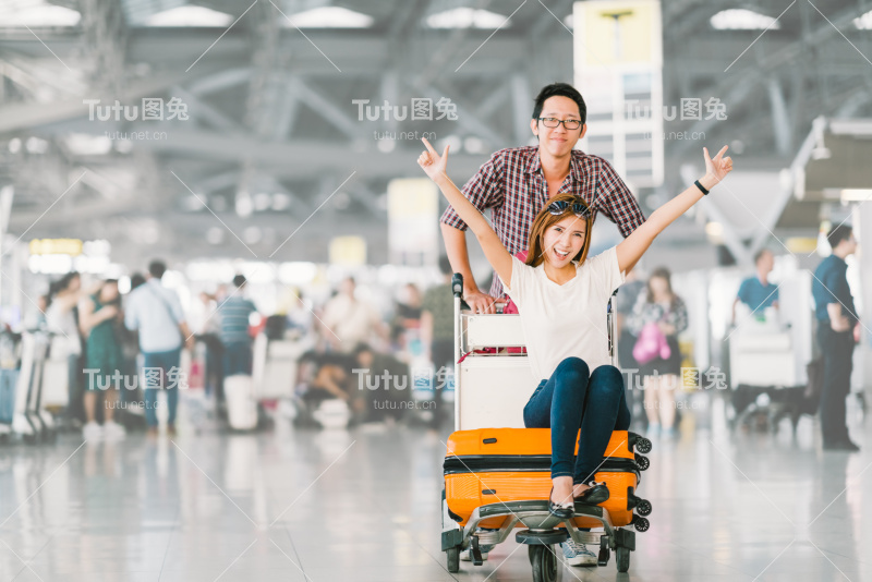 年轻的亚洲游客夫妇一起为旅行高兴和兴奋，女朋友坐在行李车或行李车欢呼。出国度假旅游理念，有文案空间