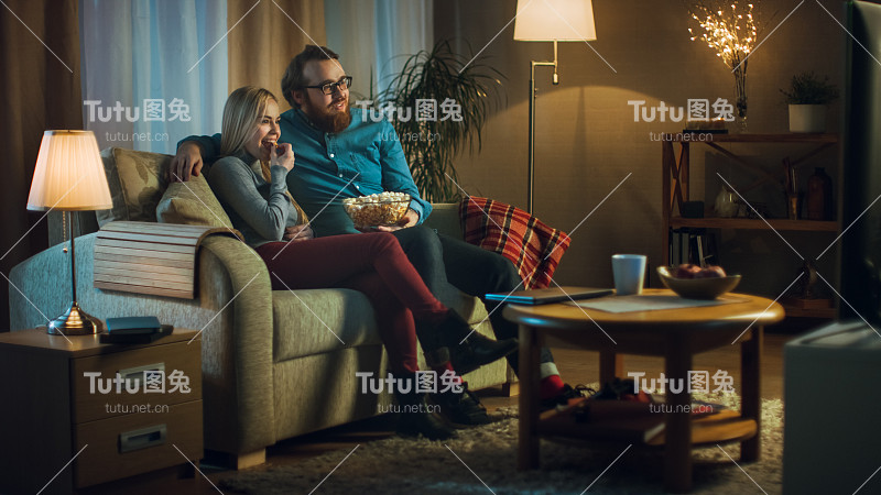 晚上，男人和女人坐在沙发上看电视和吃爆米花。客厅是舒适的。