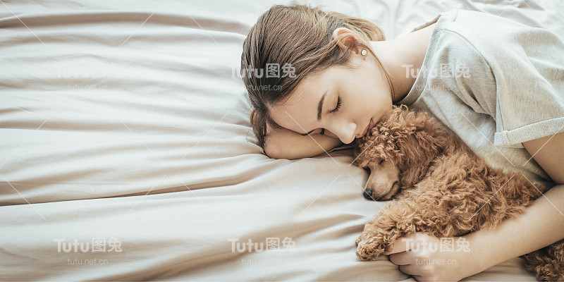 年轻女子躺在床上和狮子狗睡觉。