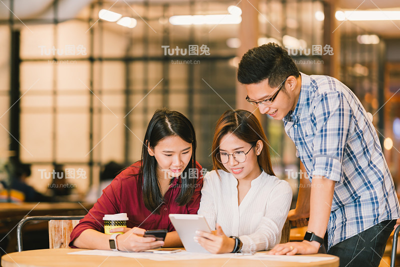 年轻的亚洲大学生或同事一起在咖啡店使用平板电脑和智能手机，多元化的群体。休闲业务，自由职业者的工作在咖啡馆，社会会议，或教育概念