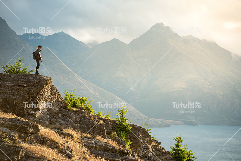 年轻的亚洲男性游客站在风景了望的边缘，背景是高山和瓦卡蒂普湖