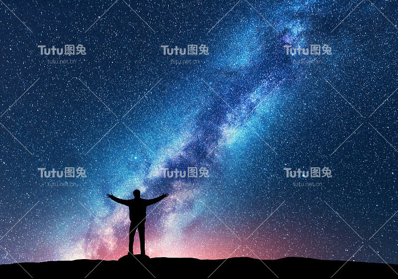 空间。银河的剪影，一个快乐的人举起手臂站在山上。夜景与美丽的银河。宇宙。夜空繁星满天，银河五彩缤纷。星空与人