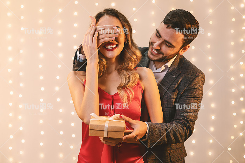优雅的男人遮住女友的眼睛，给她礼盒