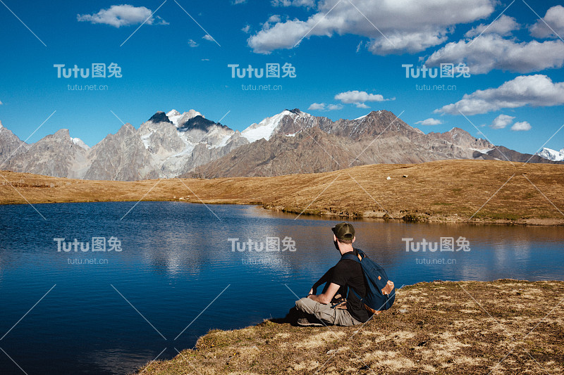 这个男人坐在湖边，欣赏着群山