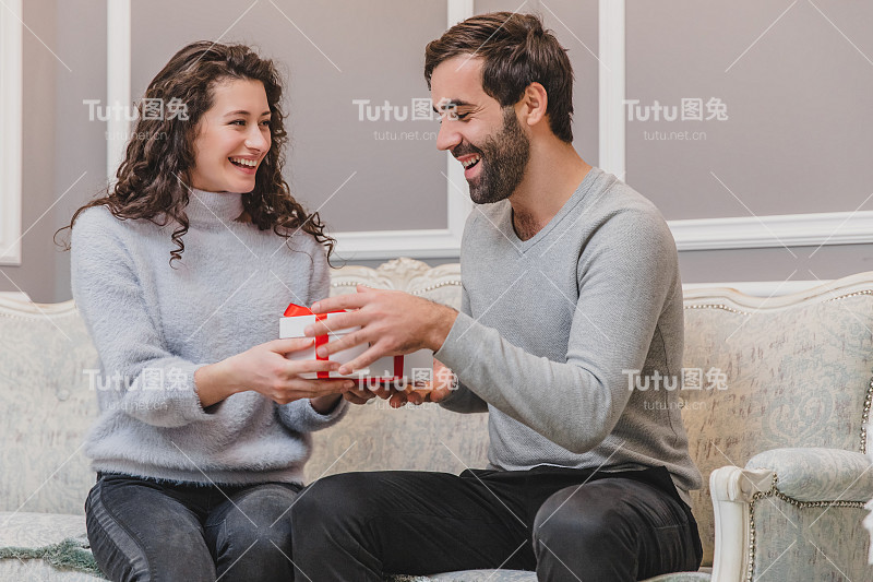 新年的时候，深情的小伙子坐在沙发上给女朋友送礼物。