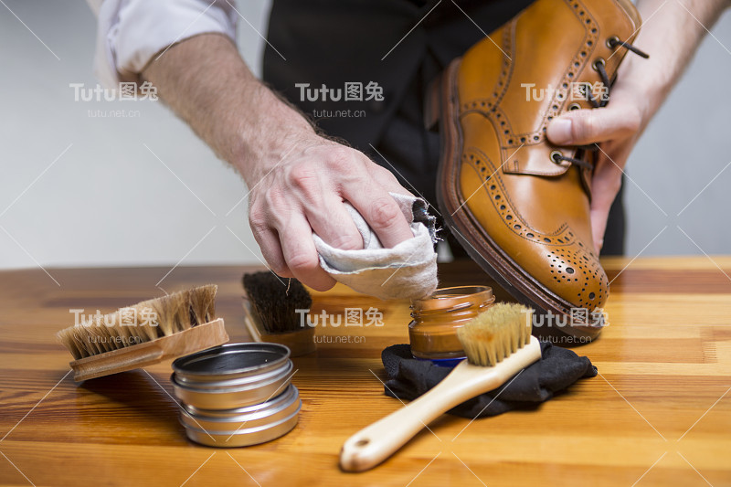 鞋类概念和想法。男人的手的特写清洁与各种刷子和配件的德比靴。水平图像组成
