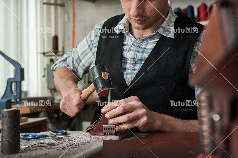 皮革工匠使用锤子与天然皮革工作的特写。