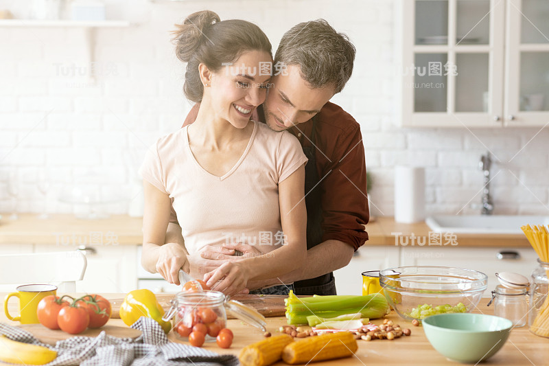 切蔬菜的时候，丈夫拥抱充满爱心的妻子
