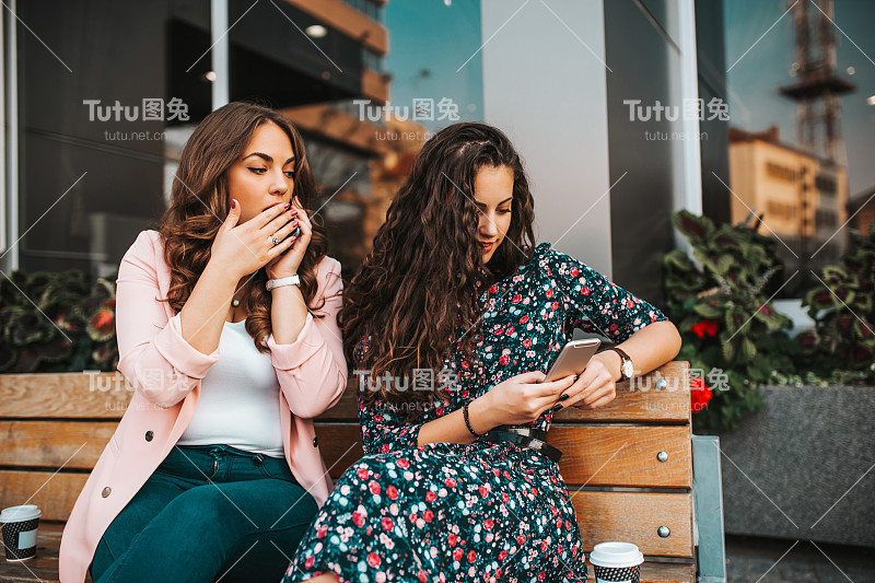 好奇的女人一边打电话一边偷看她朋友的智能手机
