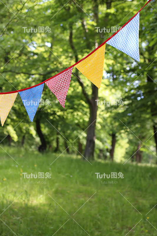 树上悬挂着五颜六色的三角形彩旗。夏日游园会。户外生日或婚礼装饰。仲夏，节日的概念。有选择性的重点。自然模糊背景。