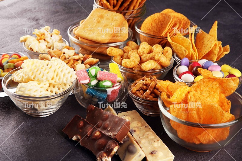 咸的零食。椒盐卷饼，薯片，饼干放在桌子的玻璃碗里