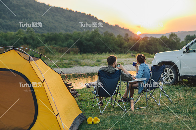 一对夫妇坐在露营椅上，看着山上河上的日落