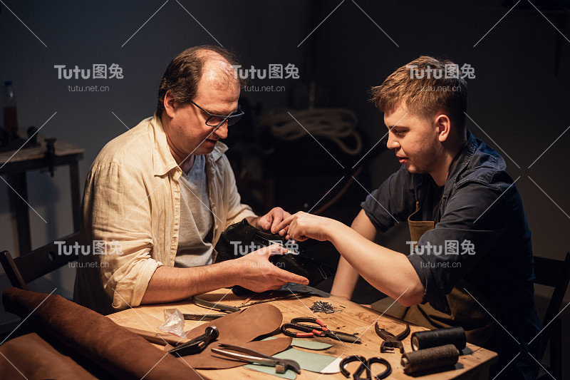 一位受人尊敬的老鞋匠在一个专门的车间为一个小男孩讲授手工制鞋的高级课程