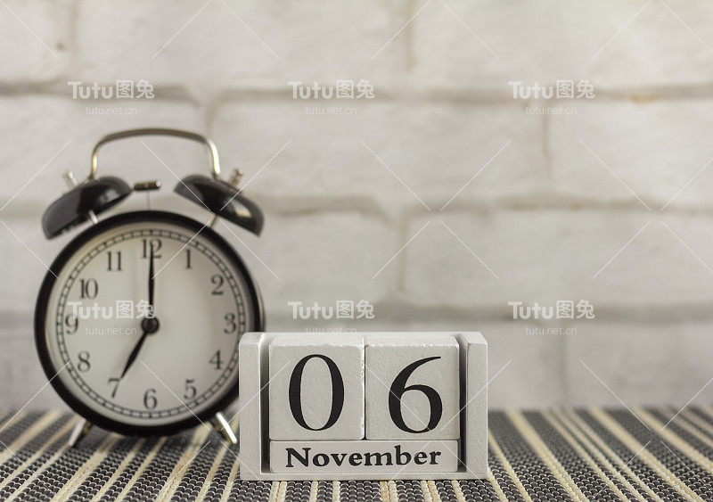 在一张黑色的桌子上，一个闹钟旁边的木制日历上写着11月6日。秋天的一天。11月份的日历。秋天