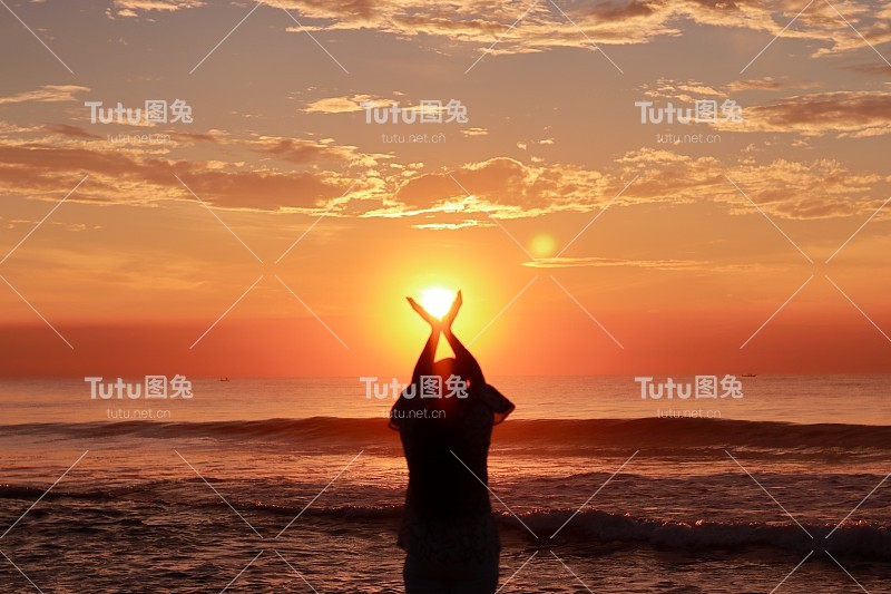 一个年轻女子的剪影，举起双手望向天空，站在日出的海边，表达她对太阳的欢迎和感激