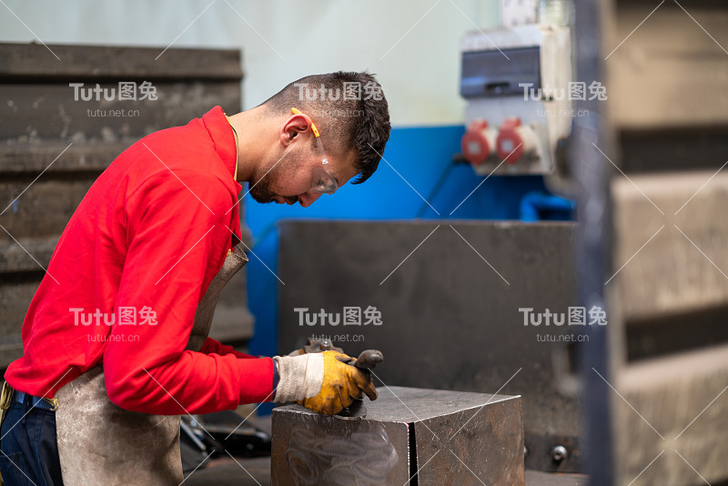 年轻的工厂工人工作时戴着护目镜和防护手套