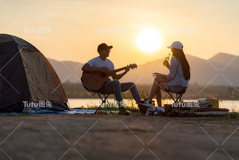 亚洲夫妇与狗弹吉他和喝啤酒旁边的帐篷营地