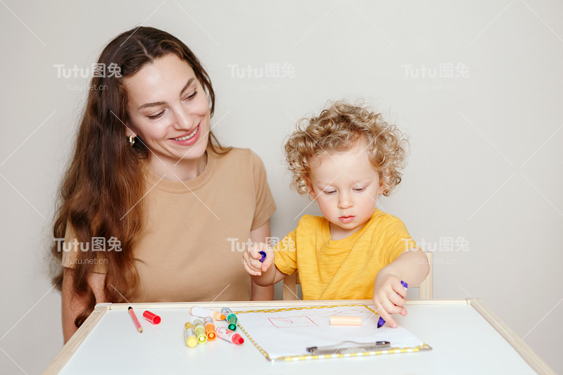 妈妈和刚学走路的小男孩一起在纸上画画。孩子用记号笔在相册里画画。幼儿教育发展学习。家庭坦率的生活在家里。