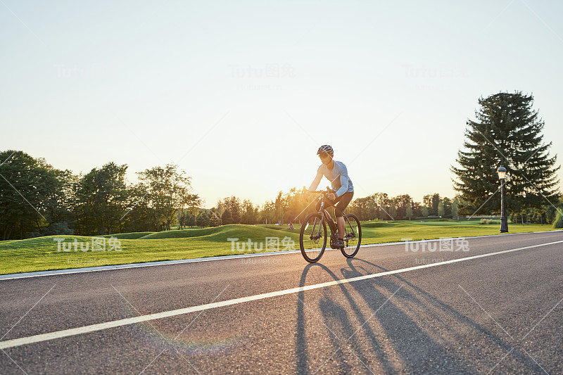 全长镜头的职业男性车手在运动服装和头盔训练，骑公路自行车在一个自行车道在公园日落