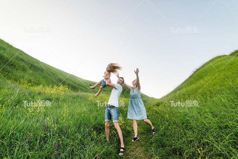 快乐的家庭在公园里。父母牵着孩子的手。妈妈，爸爸和女儿走在田野里。家庭假日的概念。