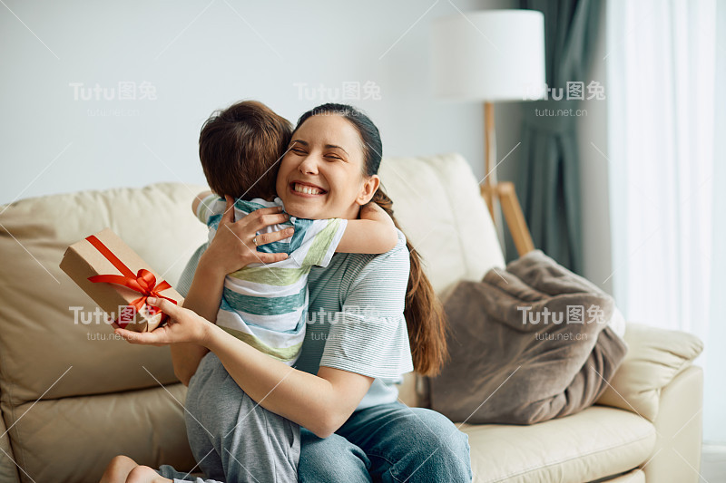 快乐的母亲拥抱她的儿子，同时收到他在家里的礼物盒。