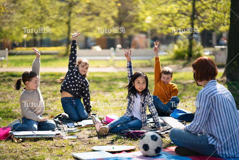 教师带幼儿坐在户外城市公园，学习小组教育理念。