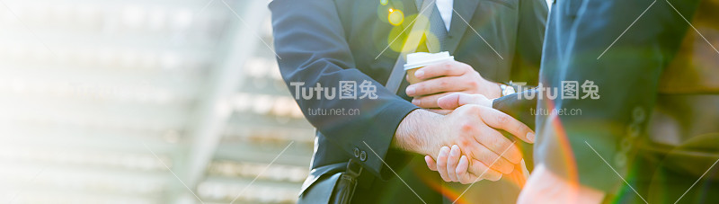 特写年轻的商业白人男子在街头城市户外用咖啡握手。团队合作友谊商人企业家合作问候头脑风暴赢得成功协同沟通概念旗帜