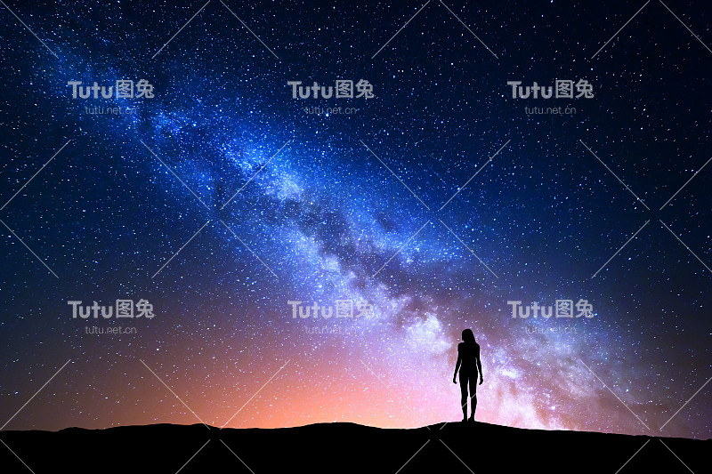 美丽的银河与站立的女人。多彩的风景与夜空与星星和一个女孩的剪影在山上的背景上美丽的银河。蓝色的银河带着黄色的光。空间