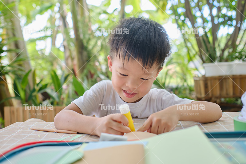 可爱快乐微笑的亚洲幼儿园孩子喜欢在家里用胶水做艺术，有趣的纸和胶水的幼儿工艺品，家庭教育的概念