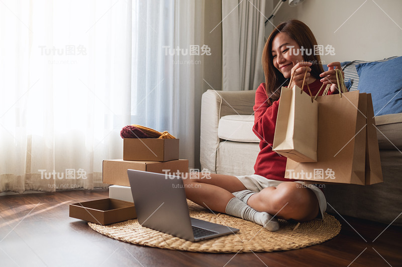 一名女子在家里用笔记本电脑网购，手里拿着购物袋，打开邮包