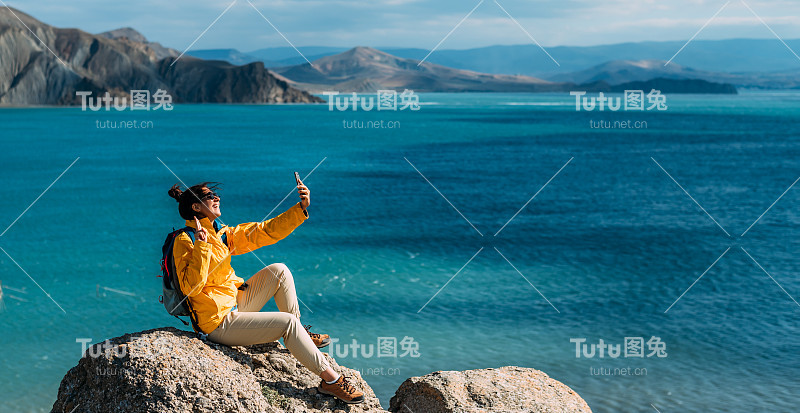 一名女旅行者正在大海的背景下进行视频通话。一名旅行者以大海为背景，用智能手机自拍。在海滨的旅行者。