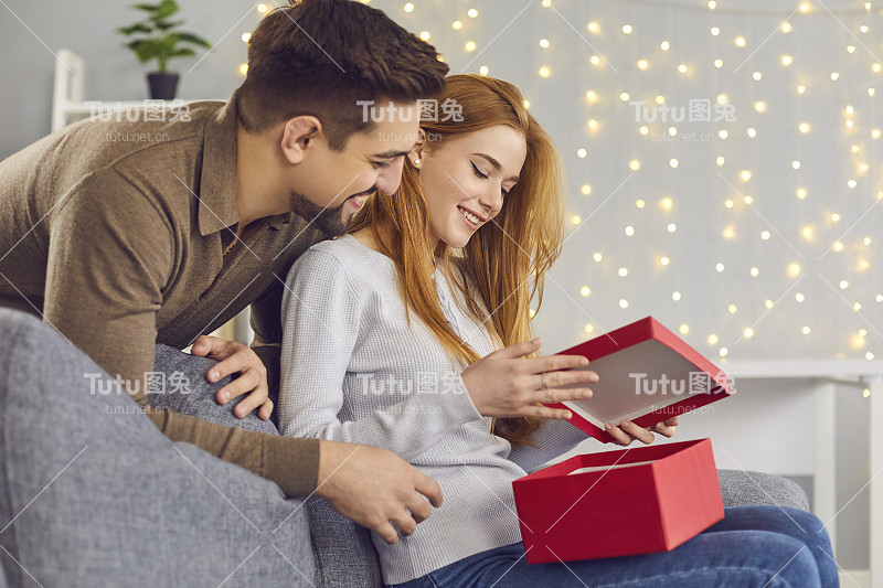 快乐的年轻女子坐在沙发上，打开男友送的情人节礼物