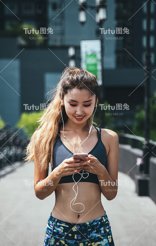 微笑的亚洲妇女在运动服装使用手机户外