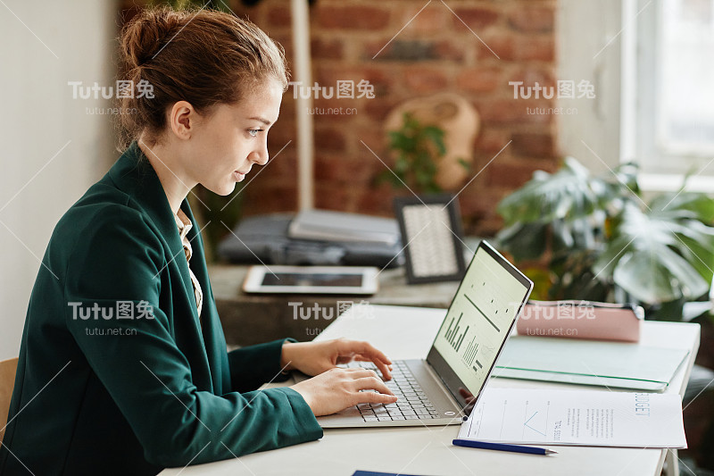 年轻自信的女商人，穿着正装，在笔记本电脑键盘上打字