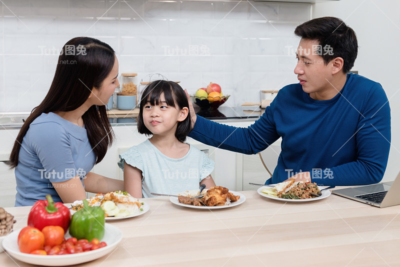 漂亮的女人英俊的男人可爱的亚洲女孩在家里的餐桌上吃饭。每个人都快乐。这对这个家庭来说是一种新的正常生活。