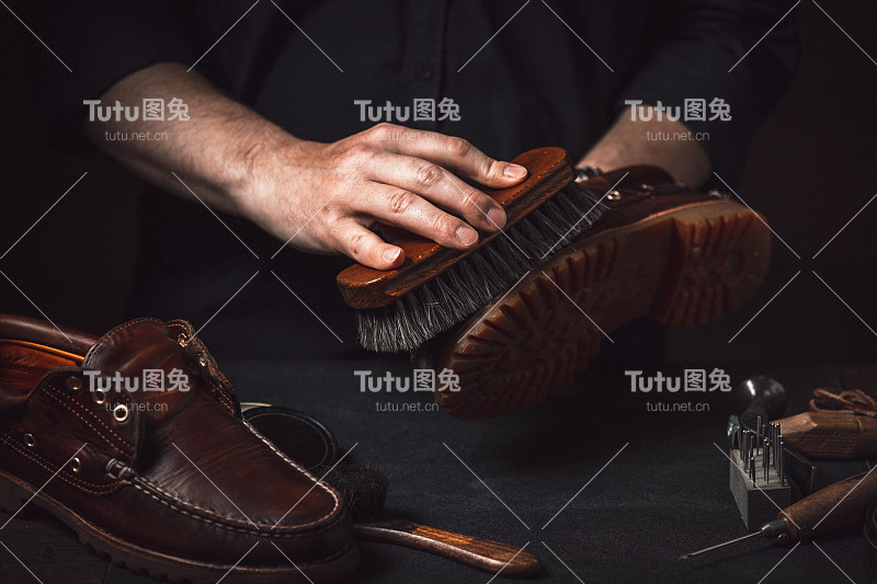 一个鞋匠在他的车间里用刷子擦靴子。擦鞋服务