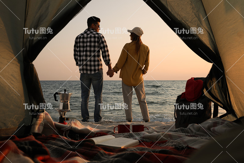 夫妇在海边日落，从露营帐篷看