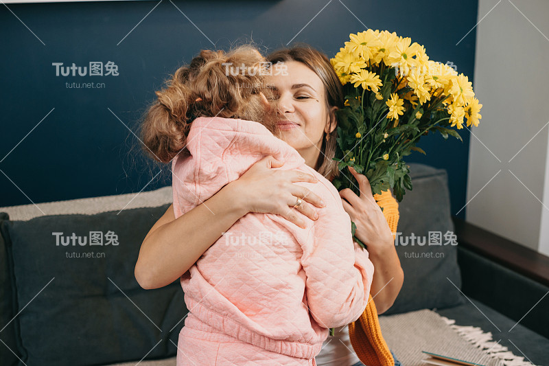 白人母亲感激地拥抱着她的小女儿，给她送花祝贺母亲节。美丽的肖像生活方式设计。微笑幸福的母女。