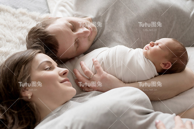 刚出生的婴儿在爸爸妈妈的怀里躺在床上。明信片母亲节和父亲节。儿童保护的一天。世界上幸福的一天。微笑的孩子。快乐的亲子关系