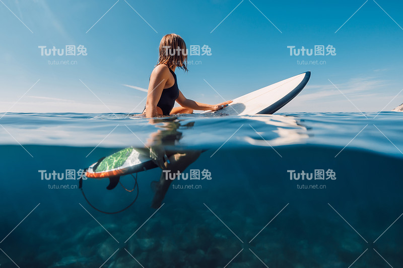 运动冲浪女孩穿着性感比基尼坐在冲浪板上，分裂的观点在海洋