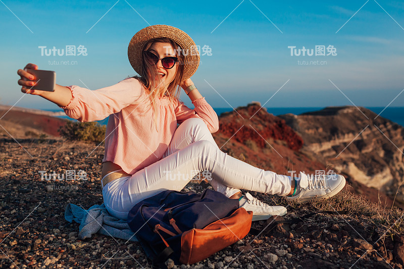 快乐的女人在海和山的背景下，在希腊圣托里尼岛自拍电话。徒步旅行者在度假