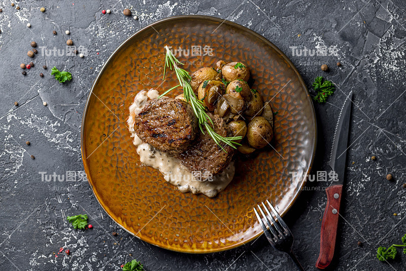 大奖章牛肉烤迷你土豆蘑菇和辣椒酱在棕色盘子上灰色的桌面视图