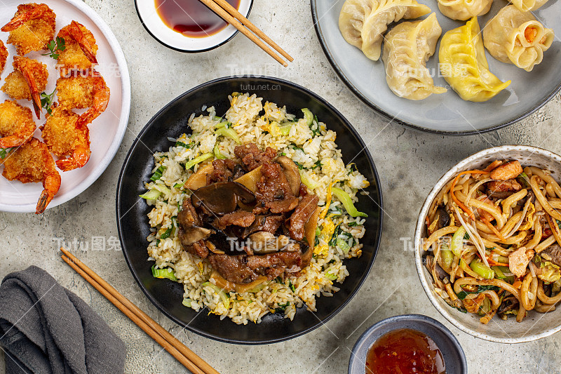 各色中国亚洲菜。餐桌上有米饭和蔬菜，炒牛肉，蔬菜，竹笋和蘑菇，炸虾，点心饺子，乌冬面，酱油和甜酱。中国餐馆的概念。