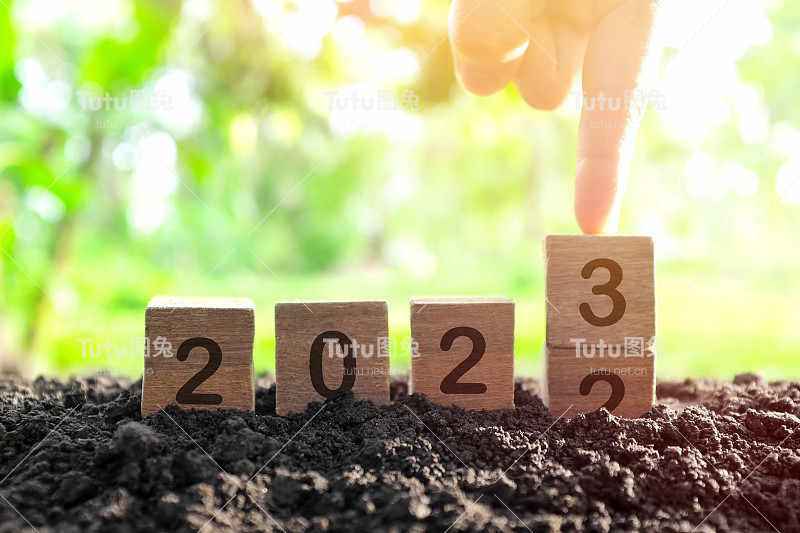 手在木块中改变2022年到2023年，在日出时种植植物。2023年新年，希望，你好和再见的概念。