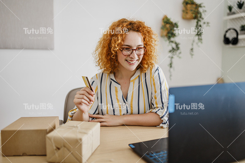 网上购物，电子商务，远程银行。年轻女子坐在家里的办公室与笔记本电脑和信用卡，在网上购买