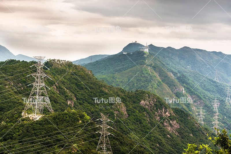 在多云的暴风雨天空下，俯瞰青山上的电力供应塔